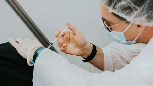 A person wearing glasses and a mask gives another person a vaccine shot.