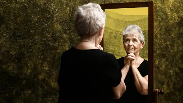 An elderly woman examines herself in a mirror