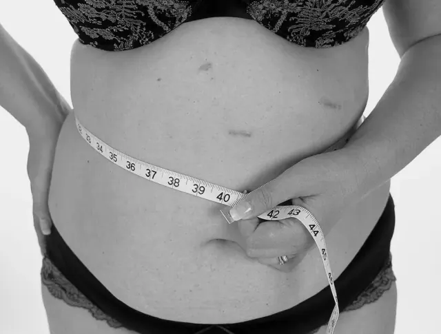 A black and white photograph of a woman holding a tape measure around her stomach