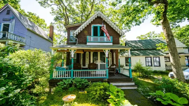 A two story wooden house with a large green porch on both levels has an American flag waving from the roof