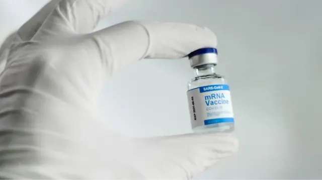 A person wearing white gloves holds a vial of a COVID-19 vaccine.