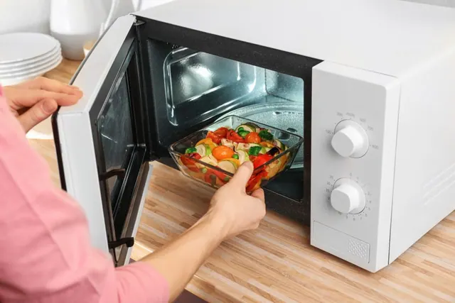 A dish being placed in a microwave in an archive kitchen photograph.