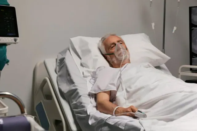An old man pictured in a hospital bed connected to breathing apparatus