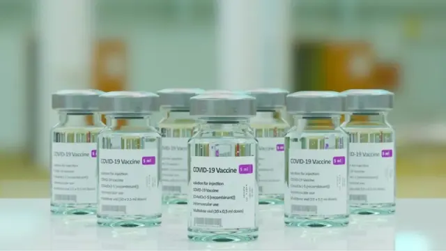 Many clear bottles of COVID-19 vaccines on a white surface, properly labeled.