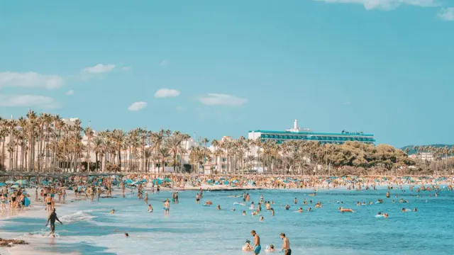 Crowded beach with people swimming and sitting on the shore.
