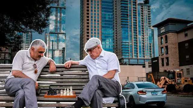 Two old men playing chess on a bench in front of a large city