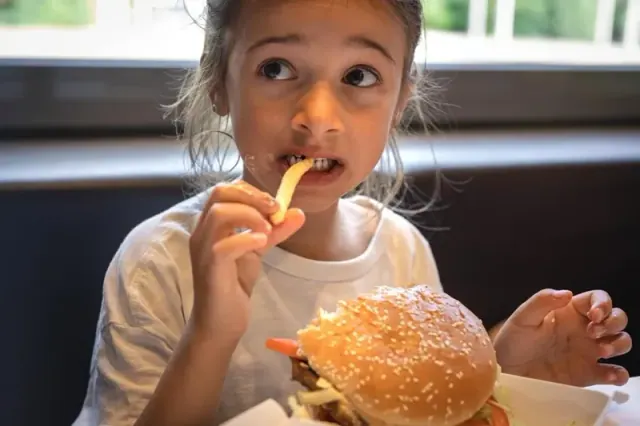 A young girl eats a hamburger and french fries
