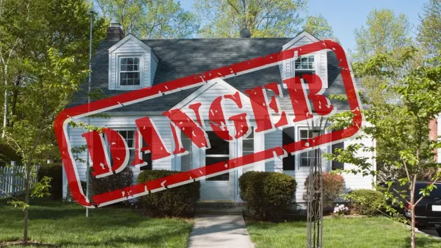 A photograph of a white house with black shutters/A red “Danger” stamp