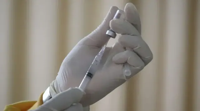 A person wearing white gloves using a needle to extract a vaccine from a bottle.