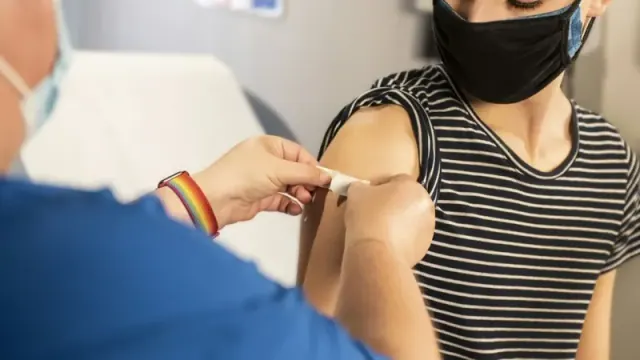 A person wearing a mask receives a bandaid over a vaccination by a health official wearing a mask.