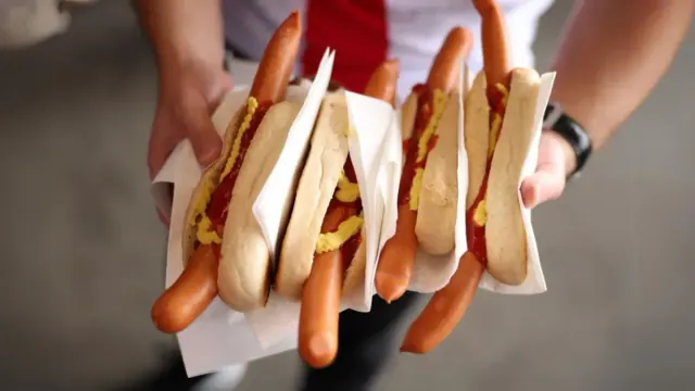 A man holds four large hot dogs with ketchup and mustard