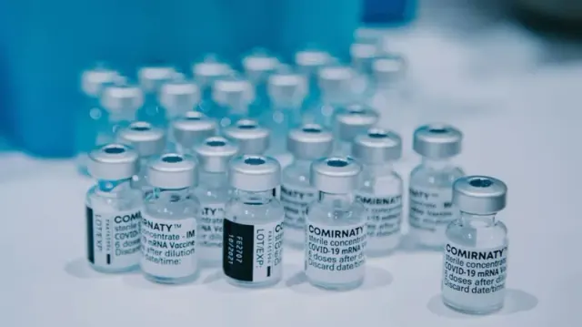Many glass bottles of COVID-19 vaccinations on a white surface.