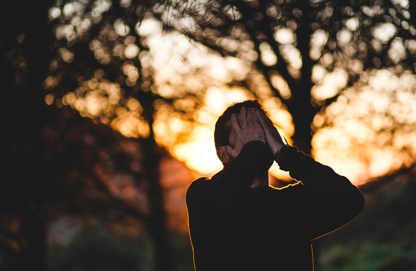A person with a hand against their face outdoors at sunset