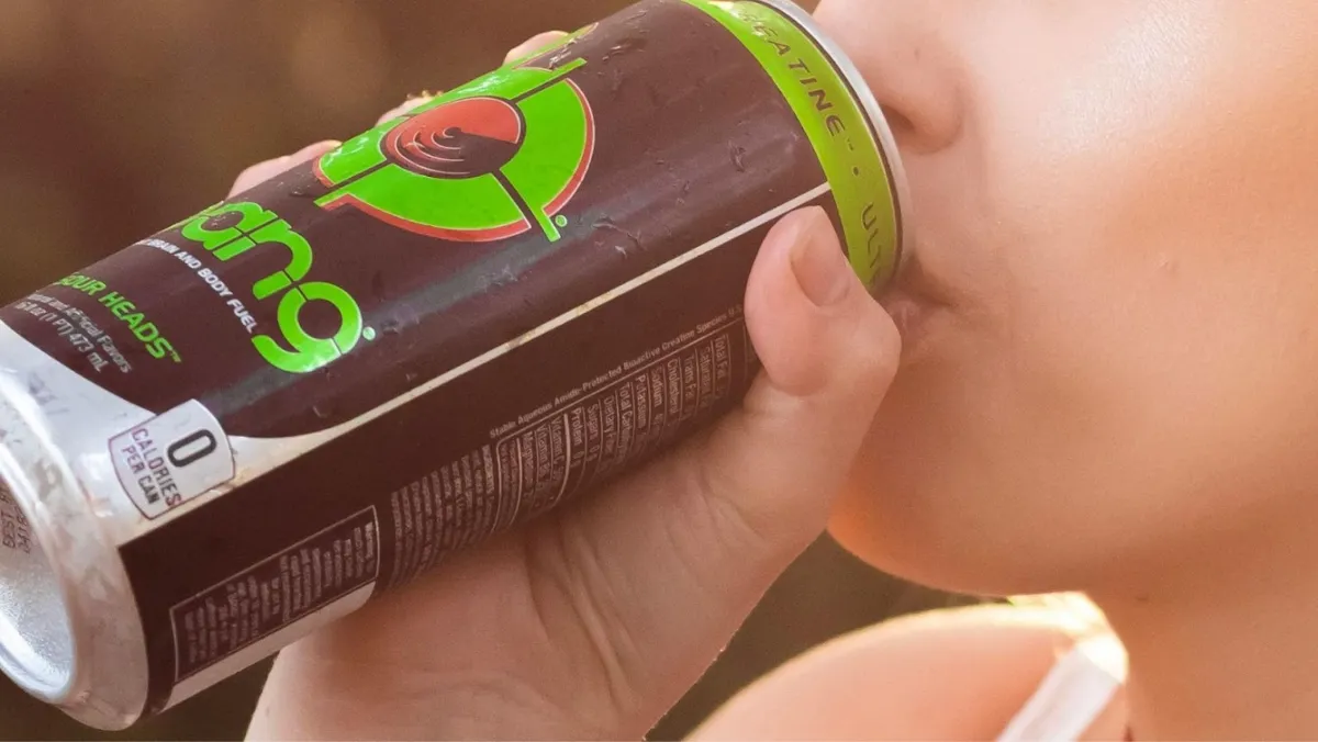 Close-up of someone drinking from a Bang energy drink can, with a focus on the can and the person’s mouth. The can is black with a bright green rim and the Bang logo in green and orange. The nutritional information is visible in small print on the can, indicating zero calories
