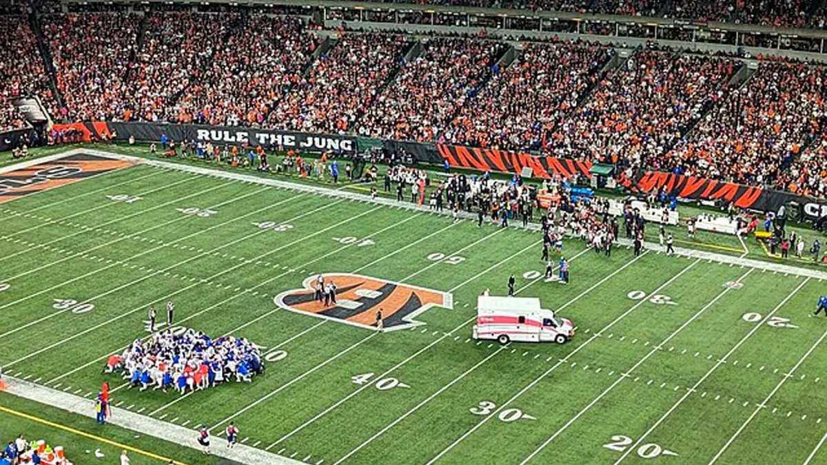 Buffalo Bills Safety Damar Hamlin is removed from Paycor Stadium in Cincinnati, Ohio in an ambulance. The Buffalo Bills, in white, kneel at the bottom left of the image.