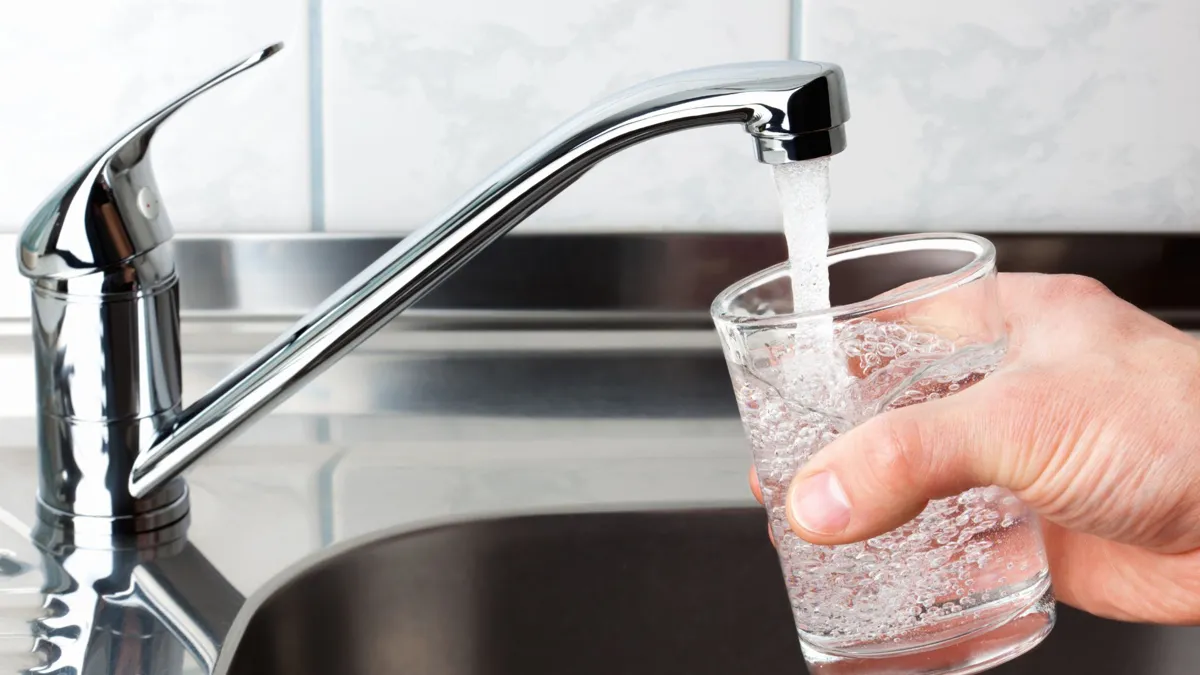 A man holds a glass of water under a faucet