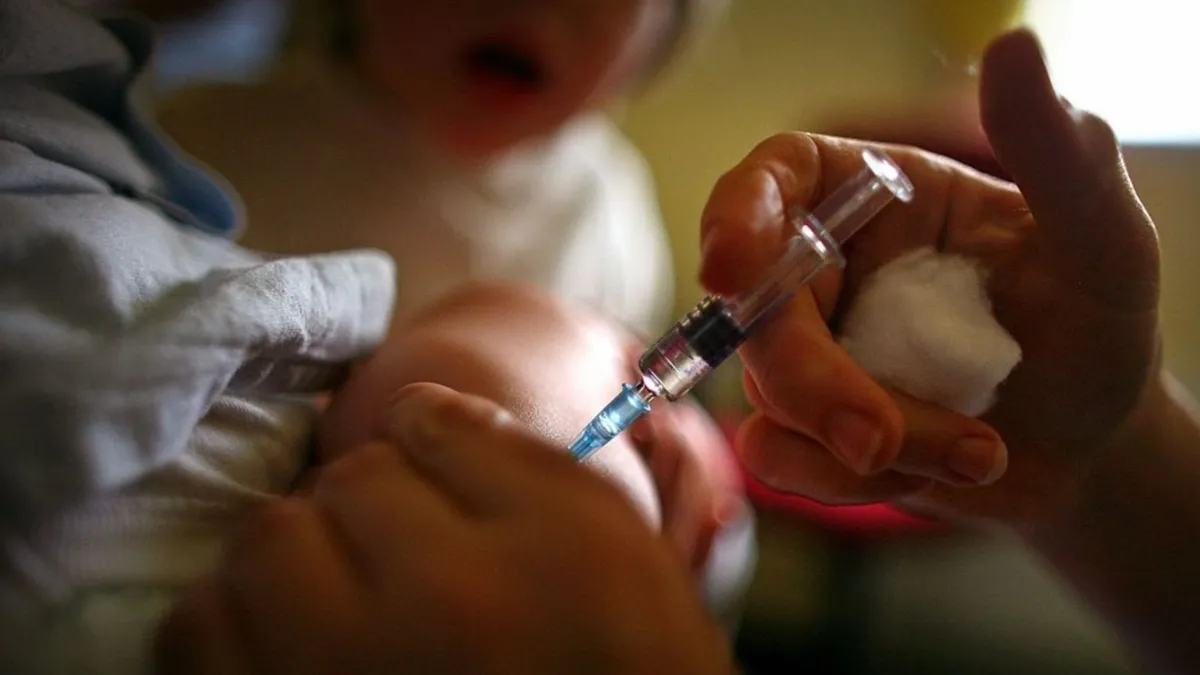 A healthcare professional administering a vaccine to a young child, with the child's arm being held steady