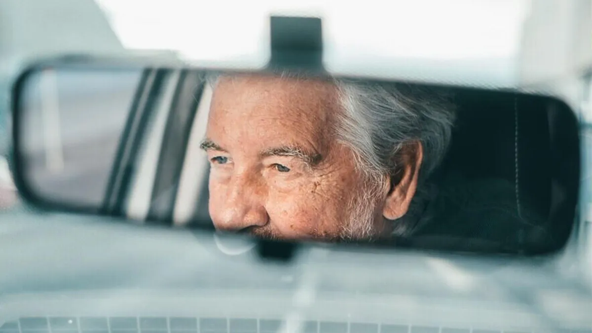 A photograph of a rearview mirror in a car showing an elderly man’s face