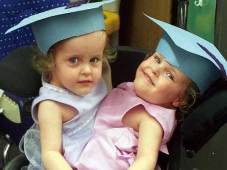 The twins wearing small graduation caps as children