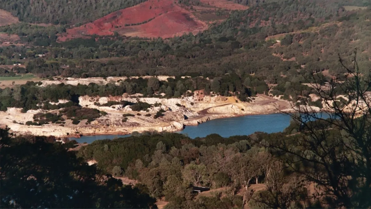 An expansive view from above shows the Sulphur Bank Mine near Clear Lake. The site features a large open pit filled with blue-green water, surrounded by barren white and tan rocky terrain