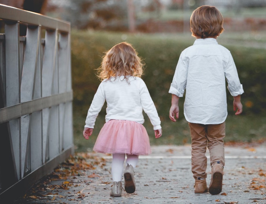 Two children walking along a path beside a fence