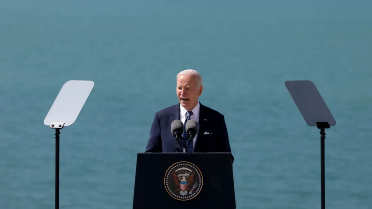 President Joe Biden stands at a podium delivering a speech in front of an ocean