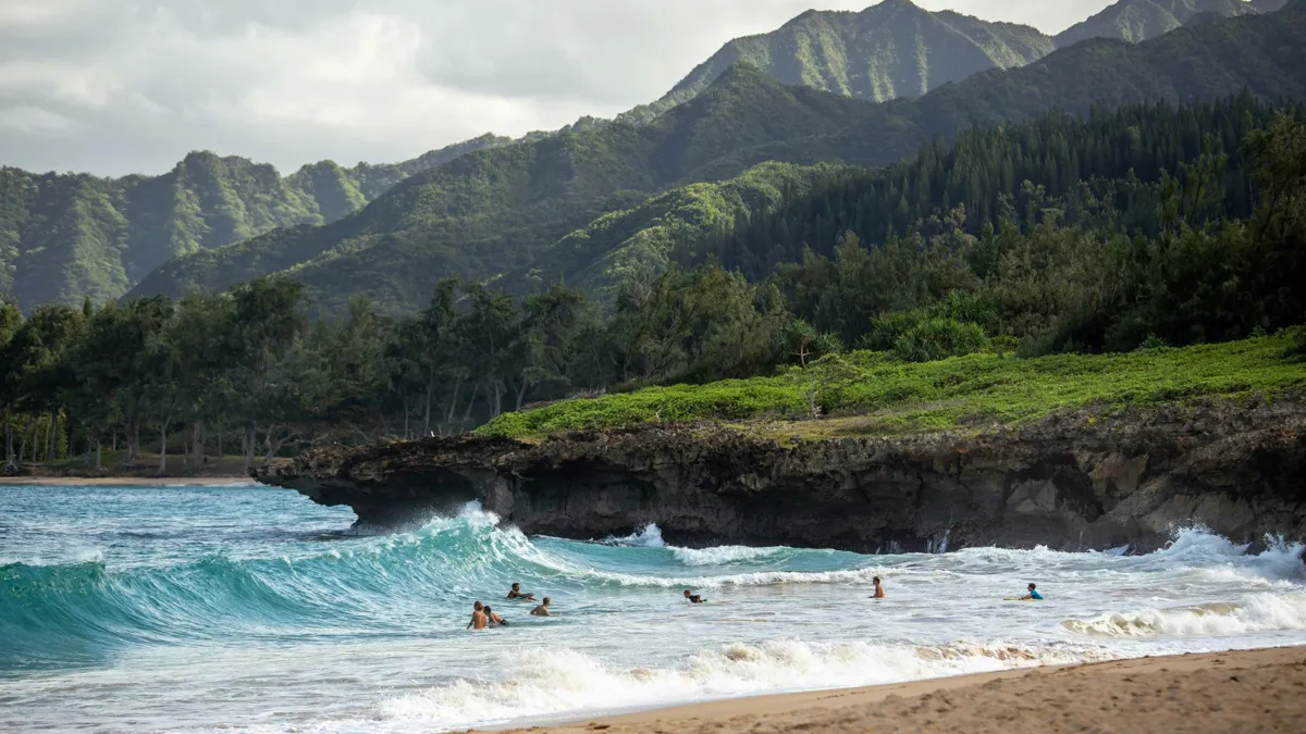 An expansive view of crashing ocean waves and forest filled mountains in the background