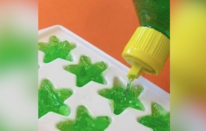 Green aloe gel being poured into a star-shaped ice tray.