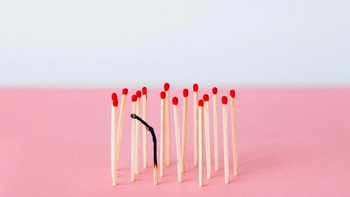 A burnt match stands atop a pink background and a bunch of regular matchsticks