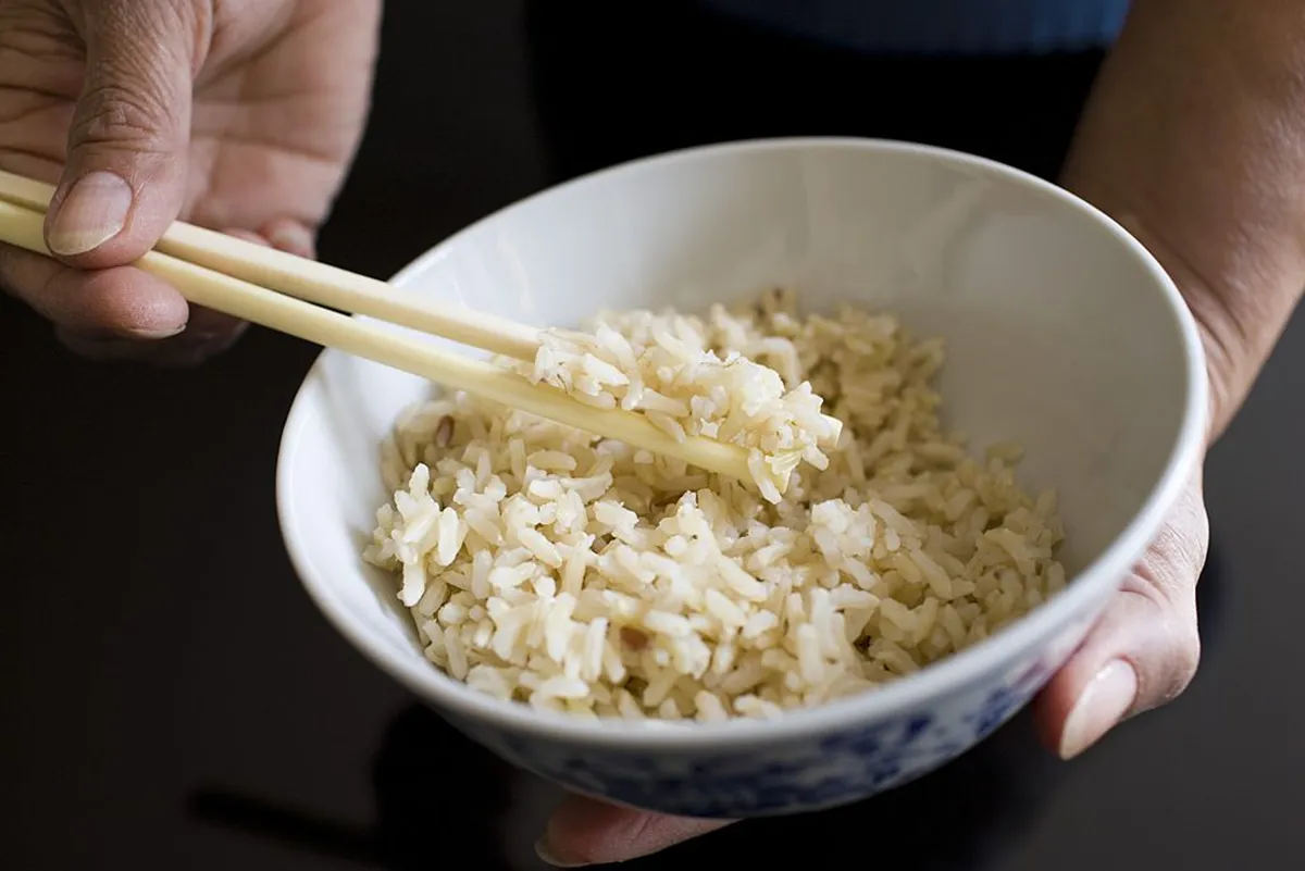 A faceless man holds a bowl of cooked rice with chopsticks