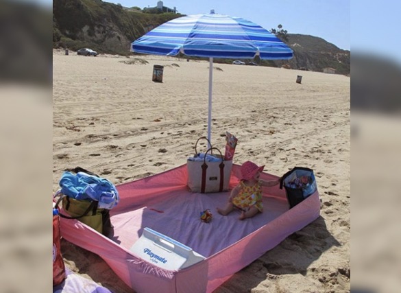 Fitted sheet arranged on sand beneath an umbrella.