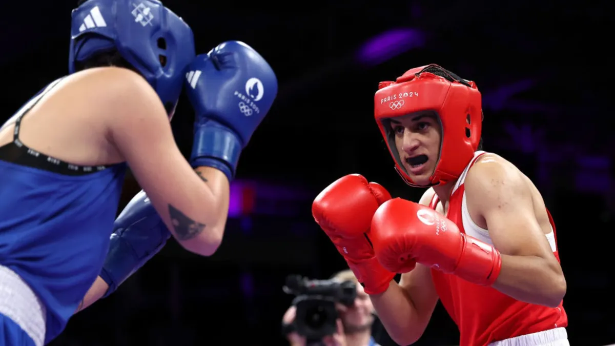 A woman in red in full boxing gear fighting a woman in blue