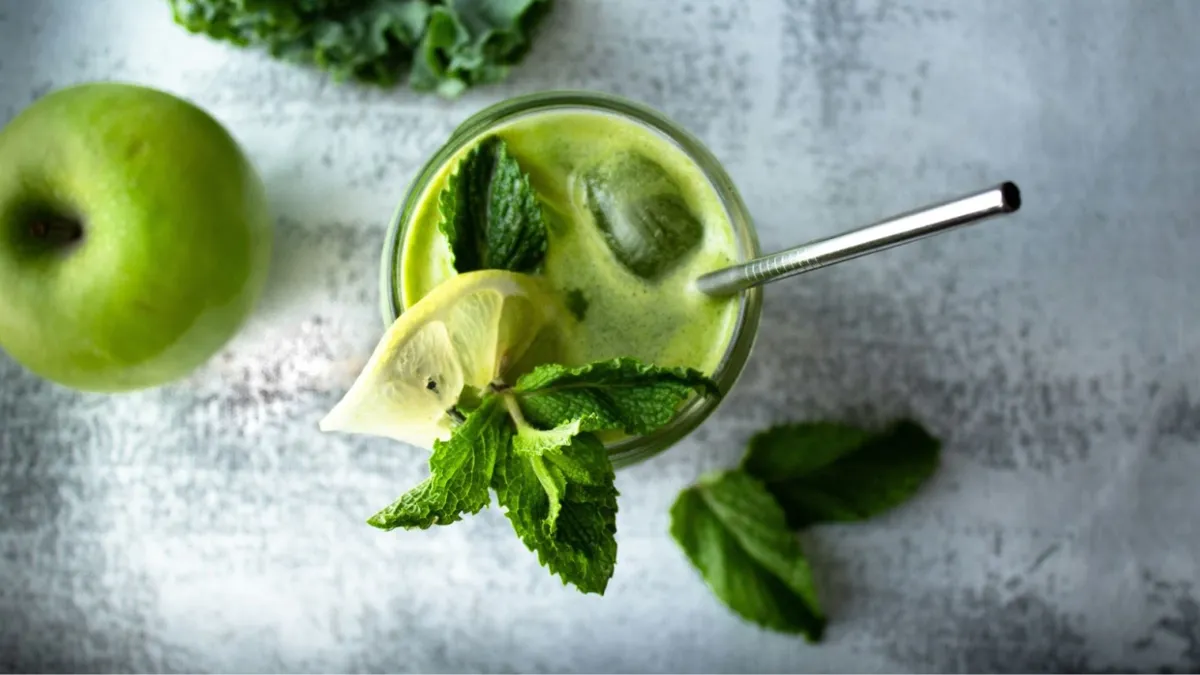 A glass with a straw full of healthy lime juice and mint, with a green apple beside the glass.
