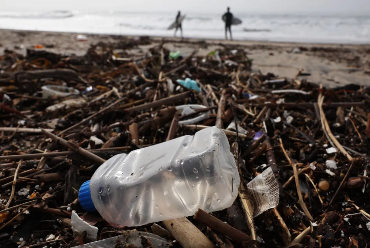 Two surfers can be seen heading to the beach in front of a plastic bottle that lies on the ground
