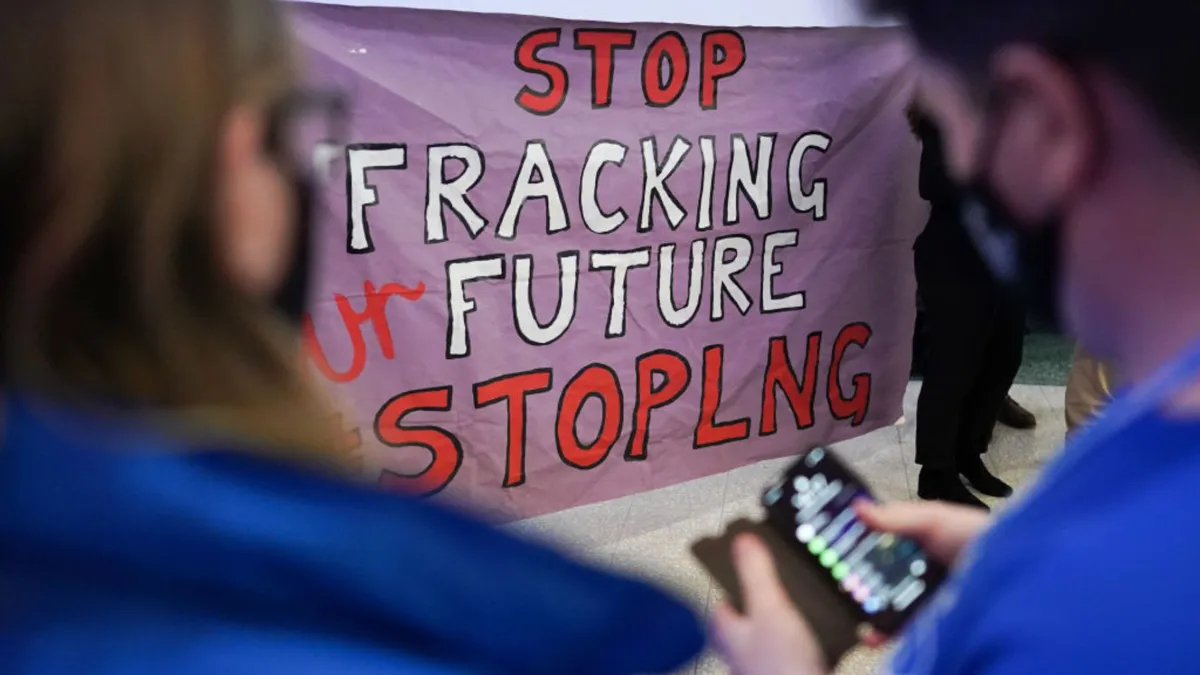 A large poster reading "STOP FRACKING FUTURE STOPLNG" is seen clearly between two people in the foreground