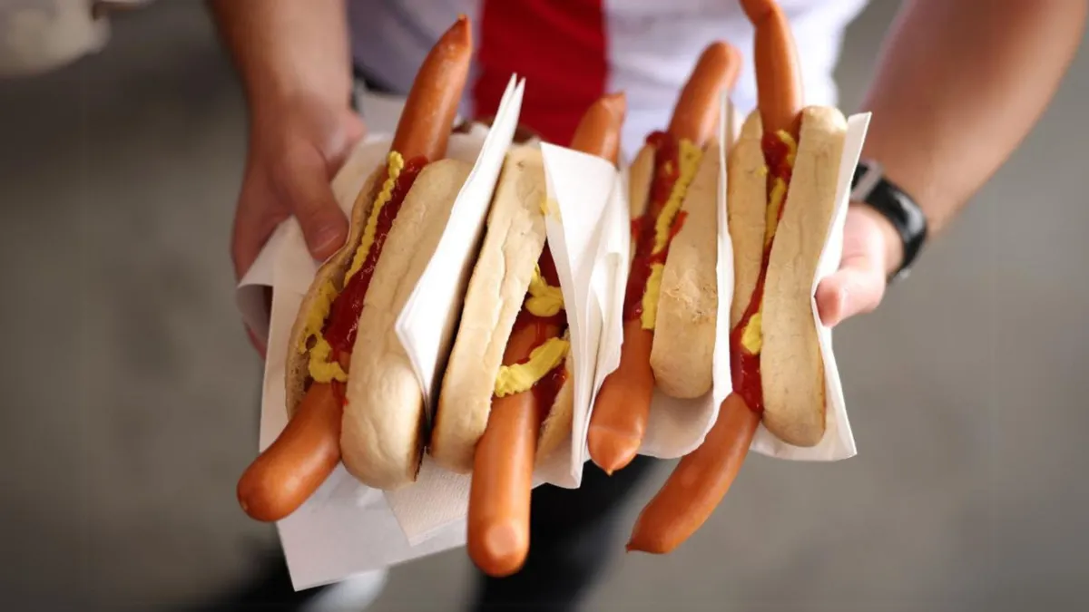 A man holds four large hot dogs with ketchup and mustard