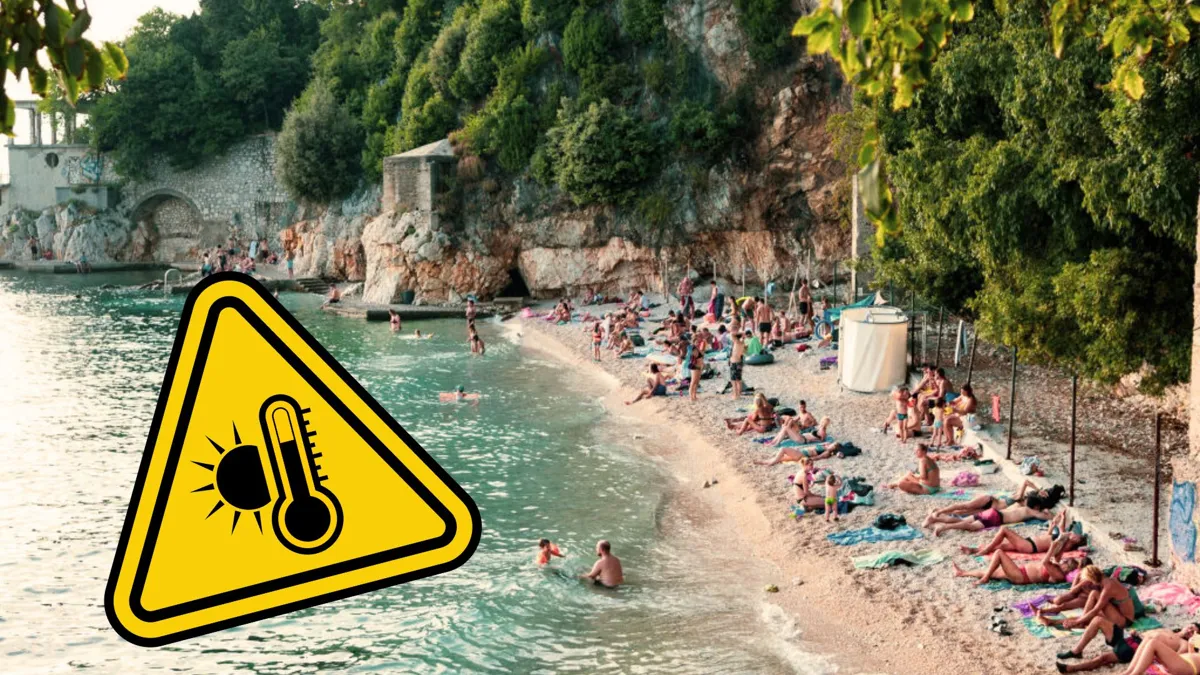 A busy beach next to a cliff with a heat warning label