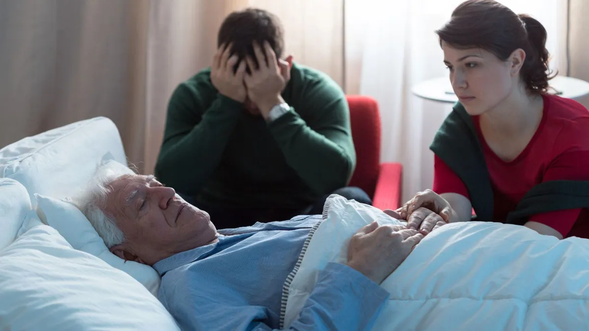 Two young people sit by their dying loved one’s hospital bed