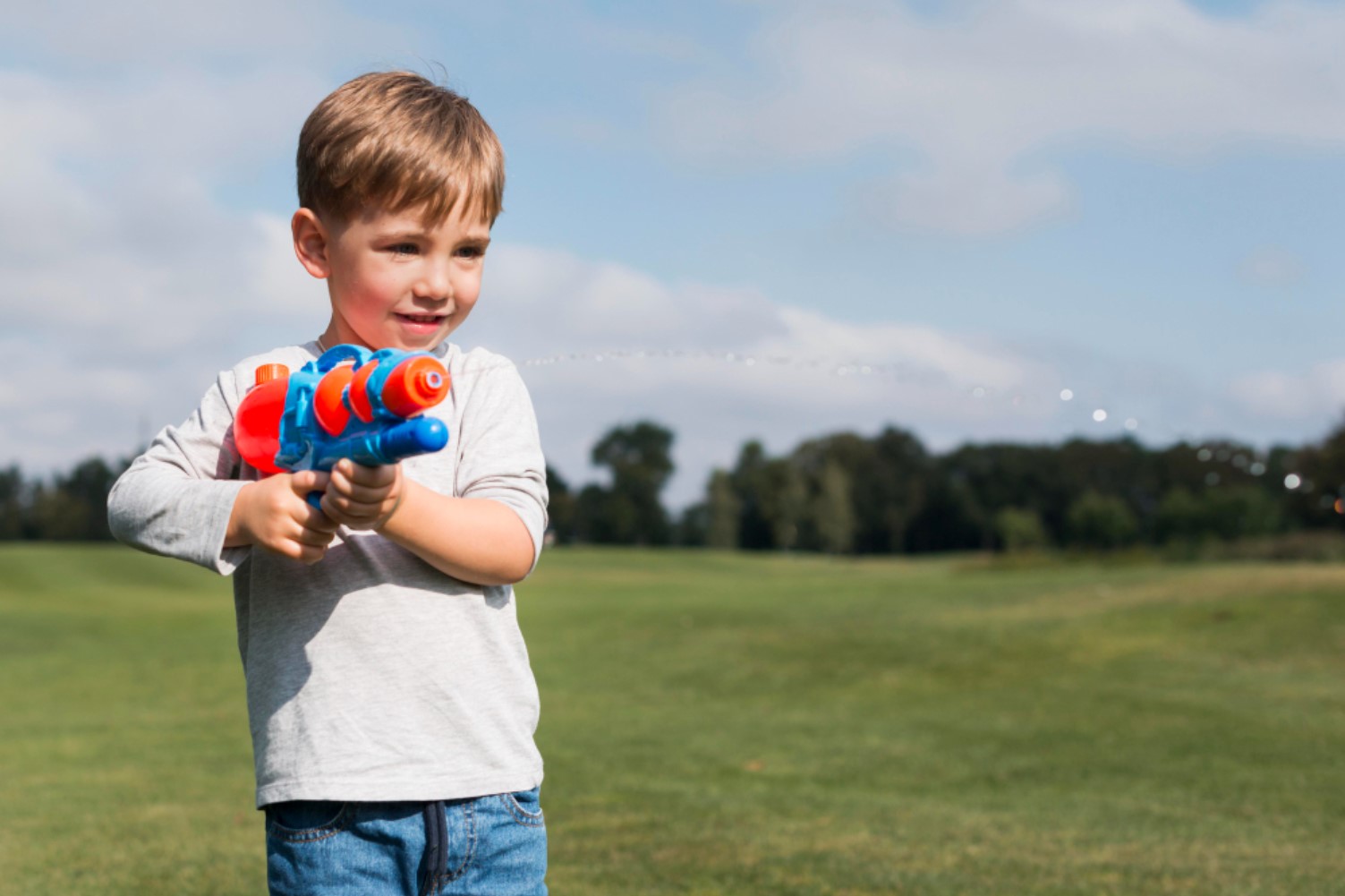 Child holding a brightly colored water pistol outdoors.