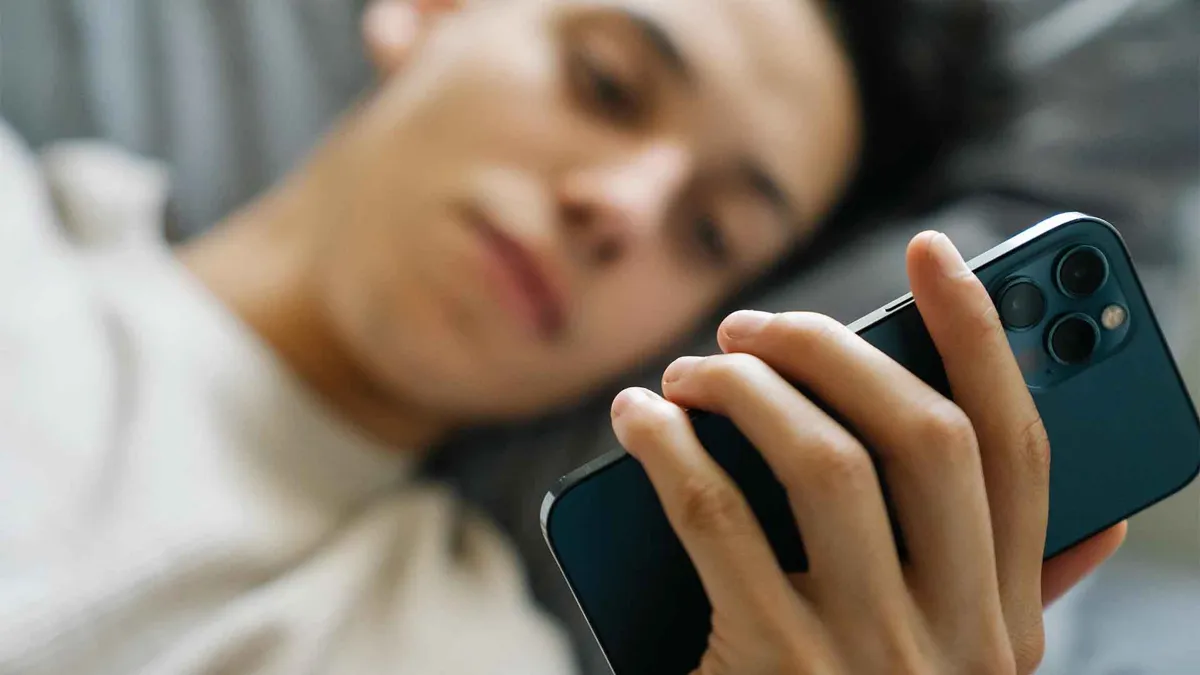 Young person browsing iPhone on bed