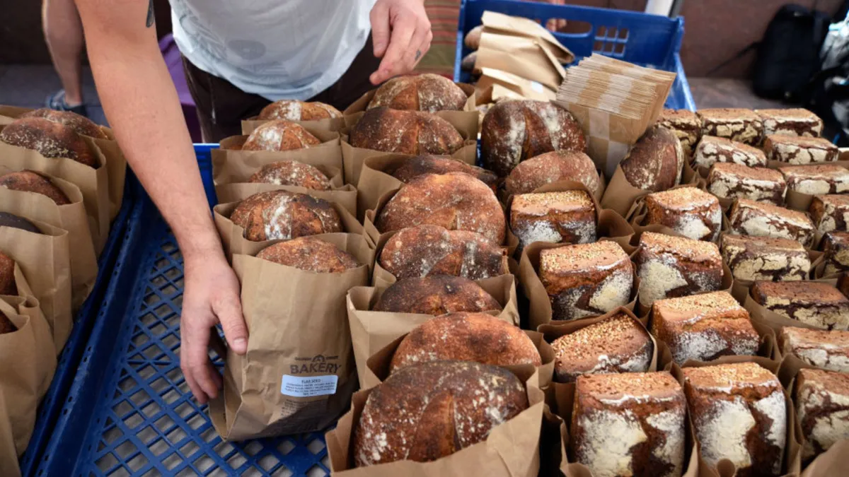A vender with several loaves of bread in brown bags on a counter