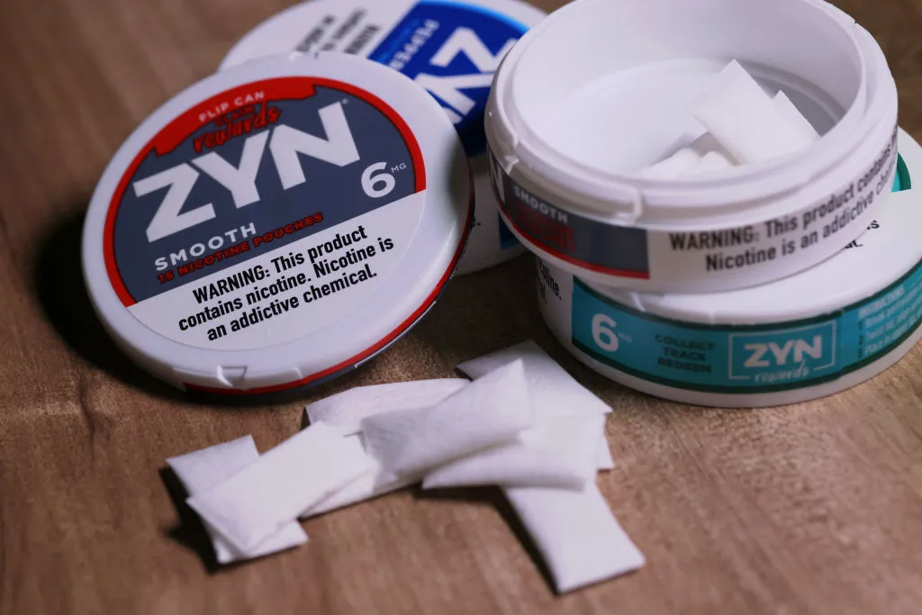 Three different flavors of Zyn Nicotine Pouches. One is open with product on the table
