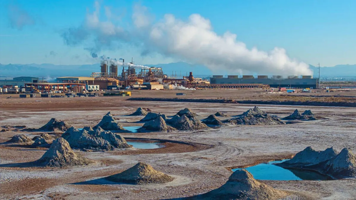 Large piles of dirt with small pools of water and a large factory in the background