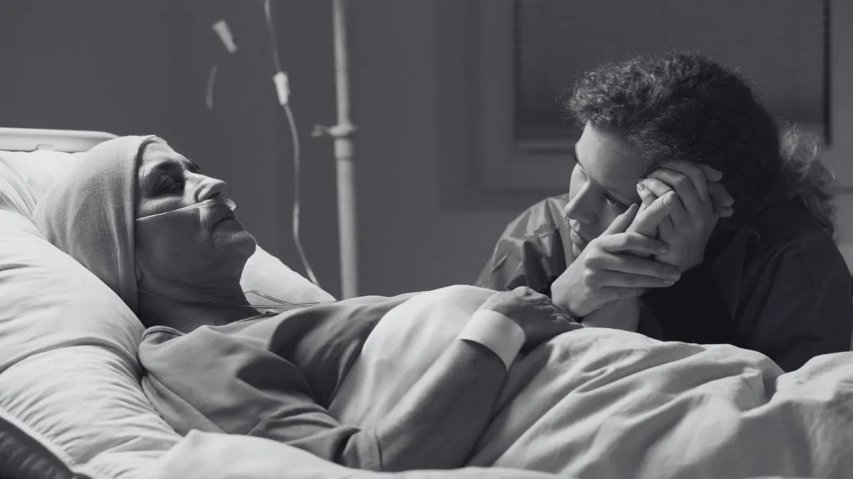 A loved one holds the hand of a patient as they lay dying in a hospital