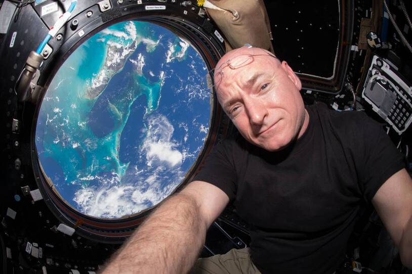 Scott Kelly beside a space-station window with Earth behind him