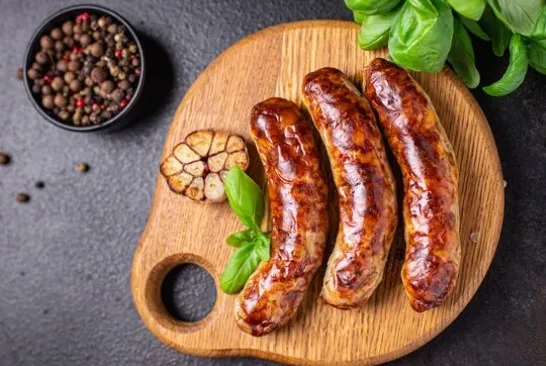 Three sausages plated on a wooden board with garlic and peppercorns at side