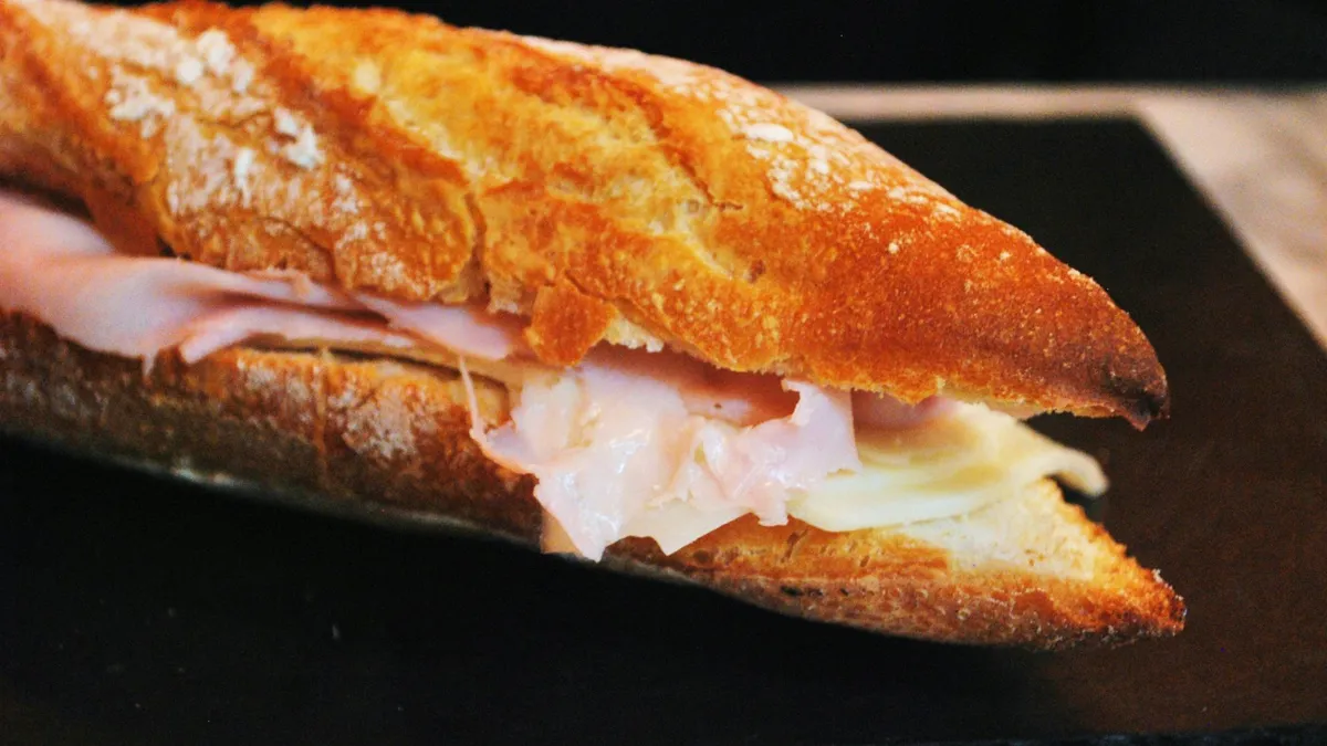 A large baguette with sliced ham and white cheese