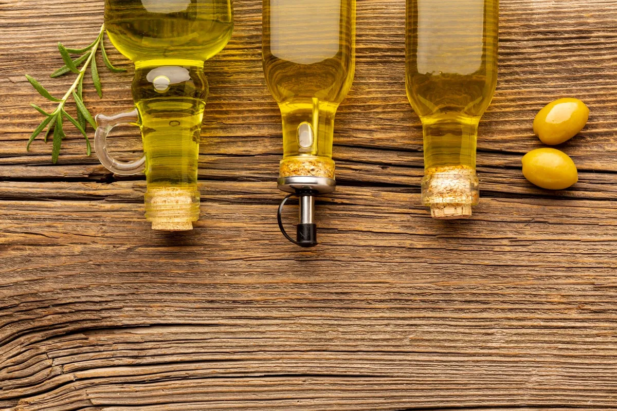 Three bottles of olive oil on a wooden table with 2 olives at the side