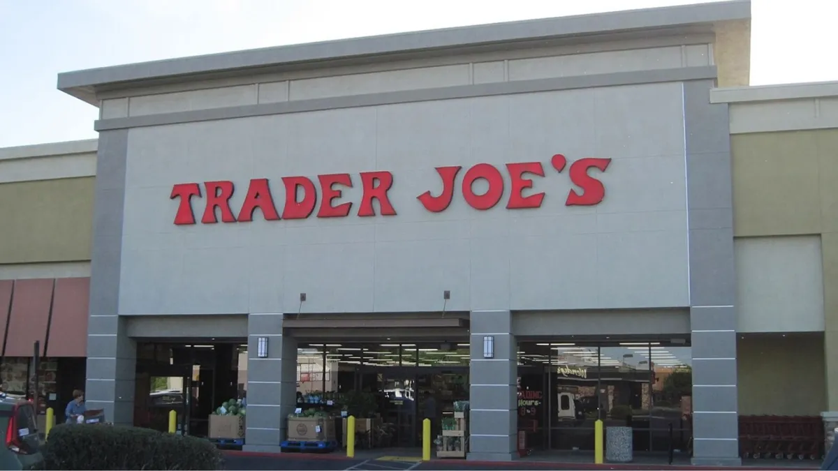Frontal image of a Trader Joe's grocery store building during daylight. The store has a large, bold red sign with 'TRADER JOE'S' in capital letters above the entrance