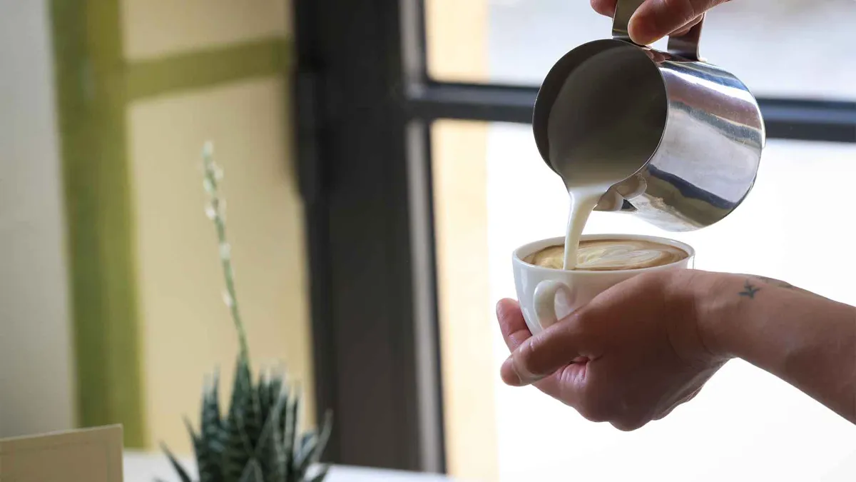Person holding mug pouring lattte into it